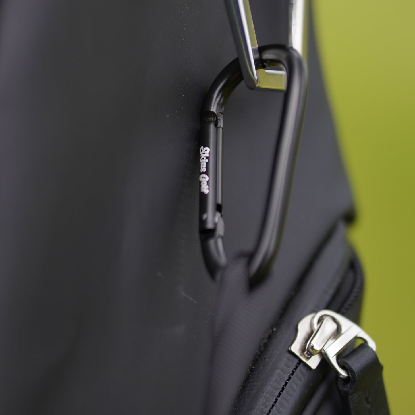 Close-up of a black bag with a carabiner and zipper detail on a green background