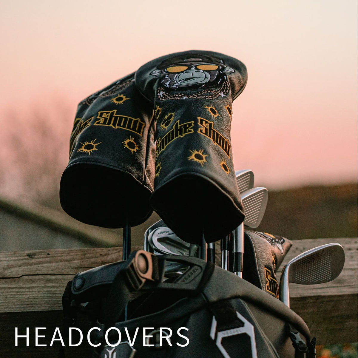 Two black golf headcovers with yellow and gray graphics on a golf bag outdoors at sunset, with the word 'HEADCOVERS' overlaid at the bottom.