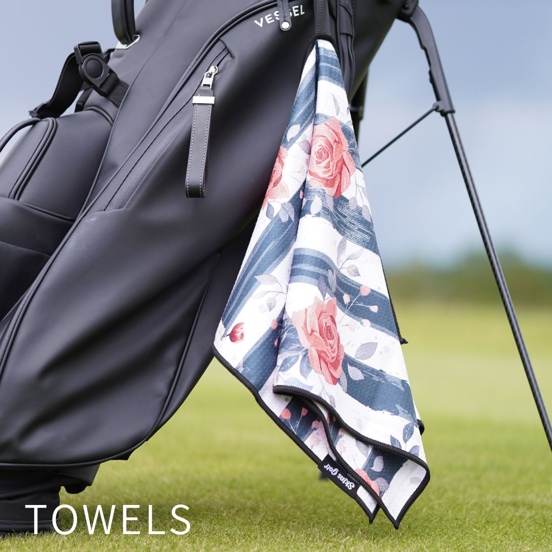 A golf stand bag on a grassy golf course with a folded towel draped over the side. The towel has a white base with blue stripes and pink rose floral patterns.