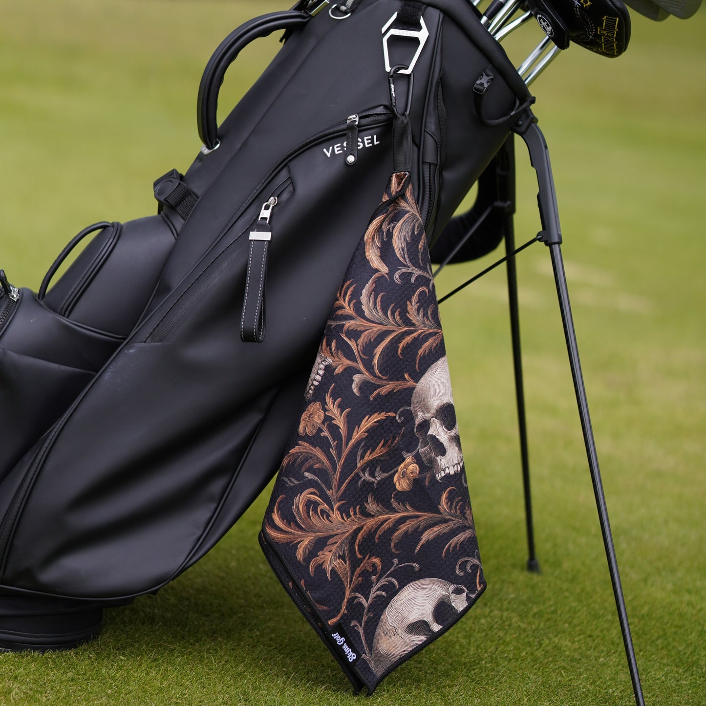 Golf bag with a decorative skull and floral patterned towel on a grassy background