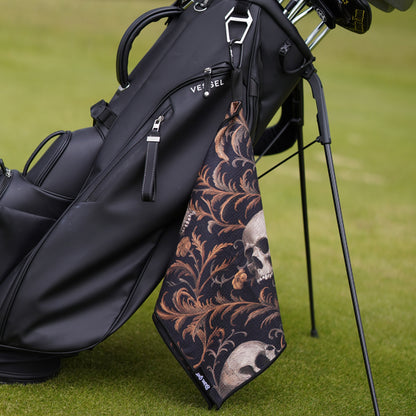 Golf bag with a decorative skull and floral patterned towel on a grassy background