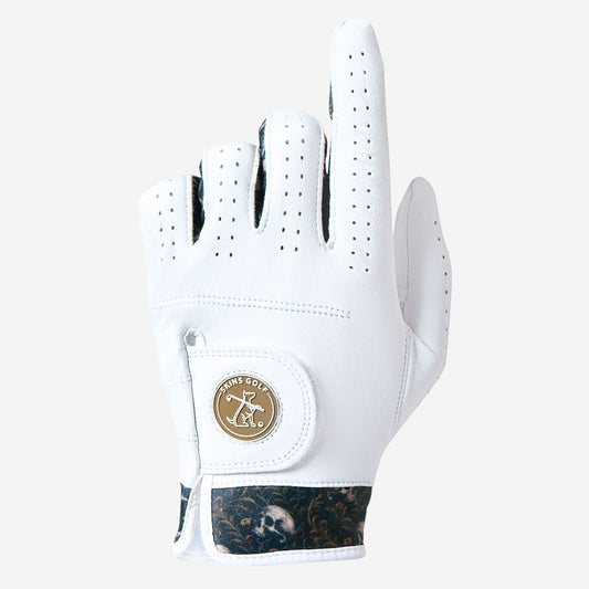 A white leather golf glove with a gold circular logo patch on the back of the hand, featuring perforated finger tips and a dark camouflage-patterned wrist strap.