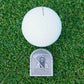 White golf ball on grass with a metal ball marker labelled 'MAKE IT'.