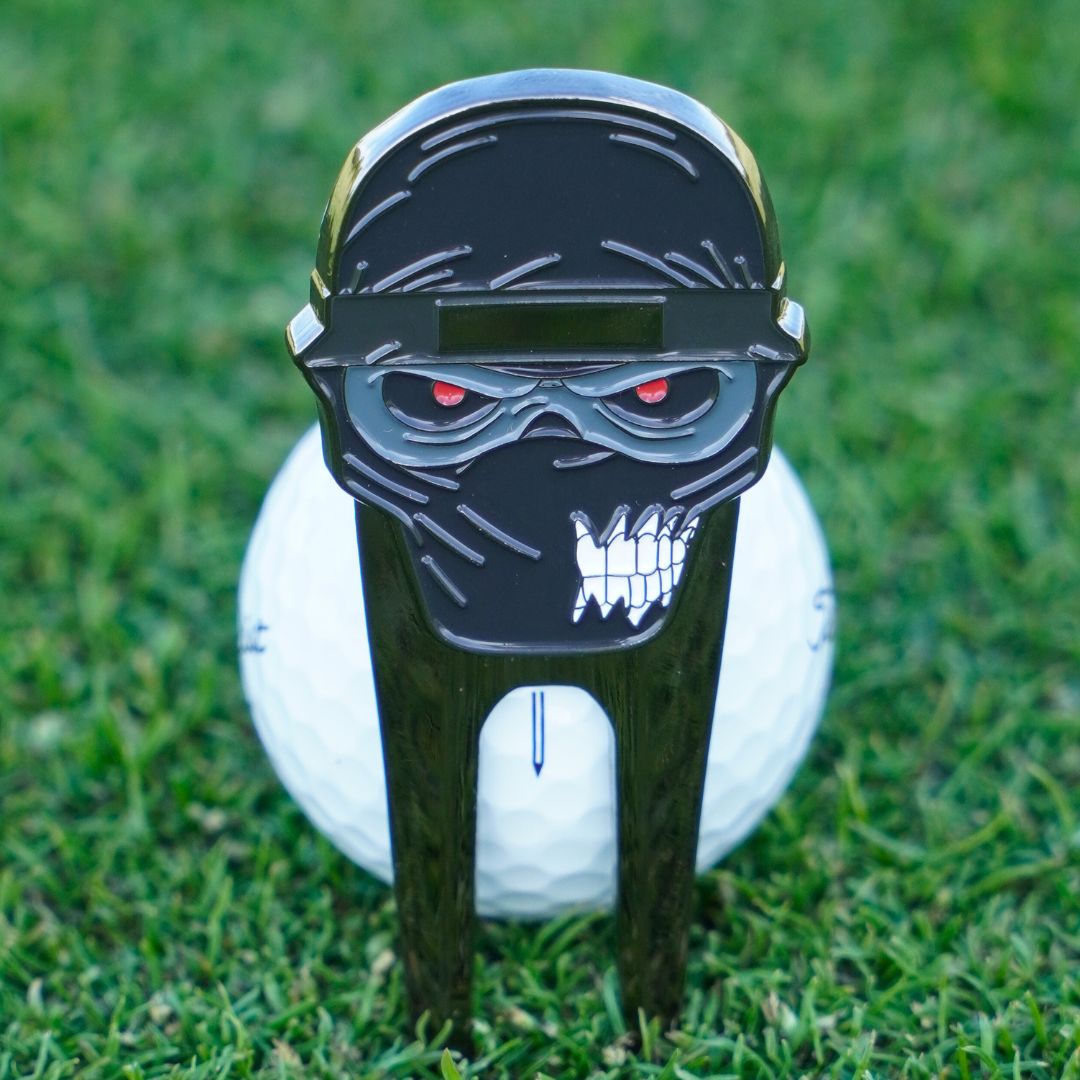 Golf ball with a ninja-themed divot tool on grass