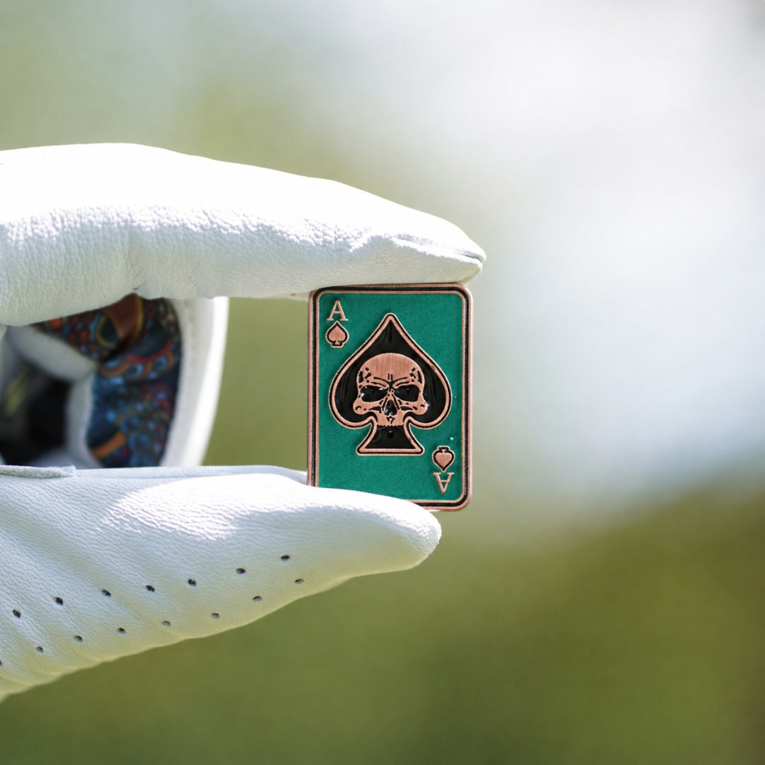 Golf ball marker with skull design held by a gloved hand against a blurred background