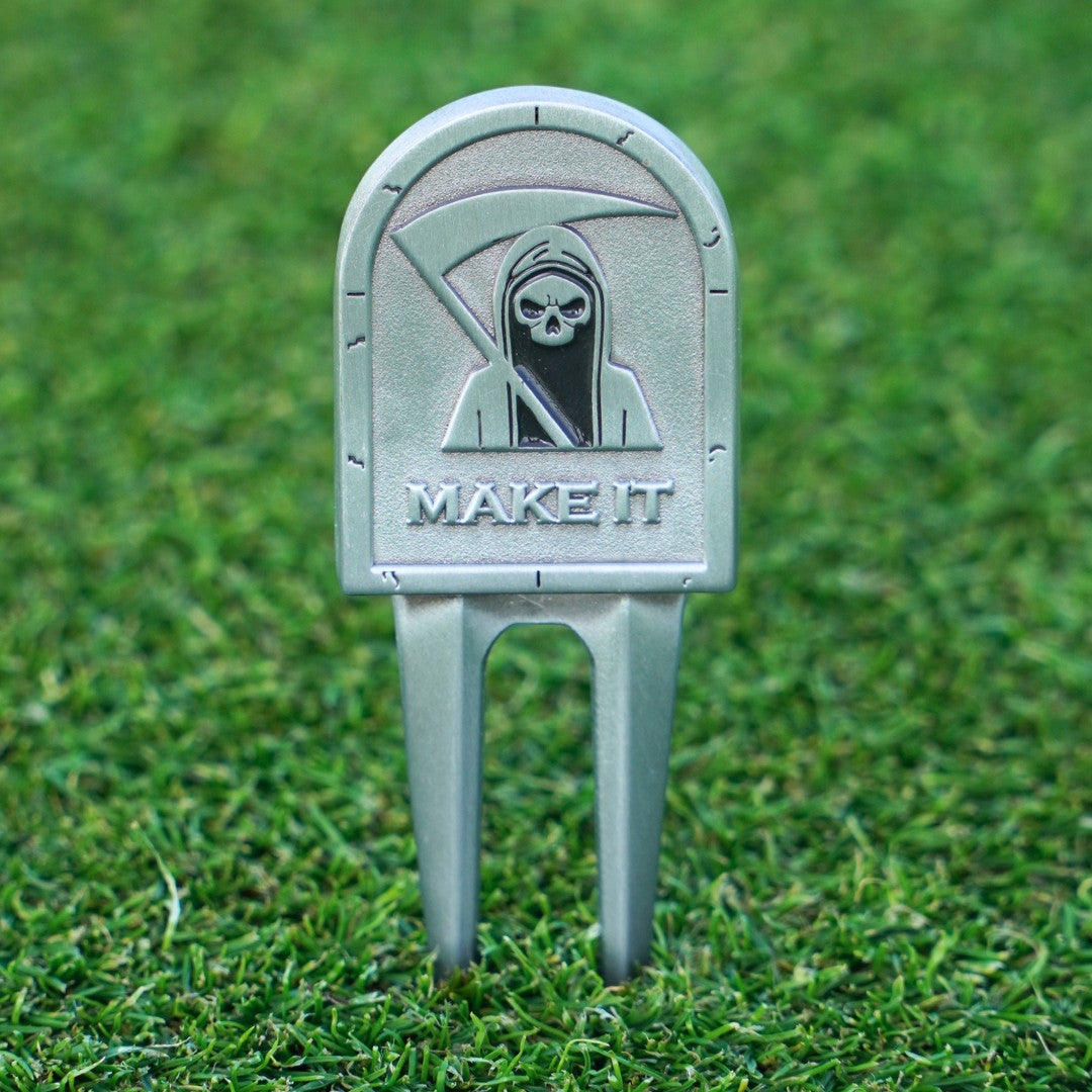 Golf divot tool with grim reaper design and 'MAKE IT' text on grass
