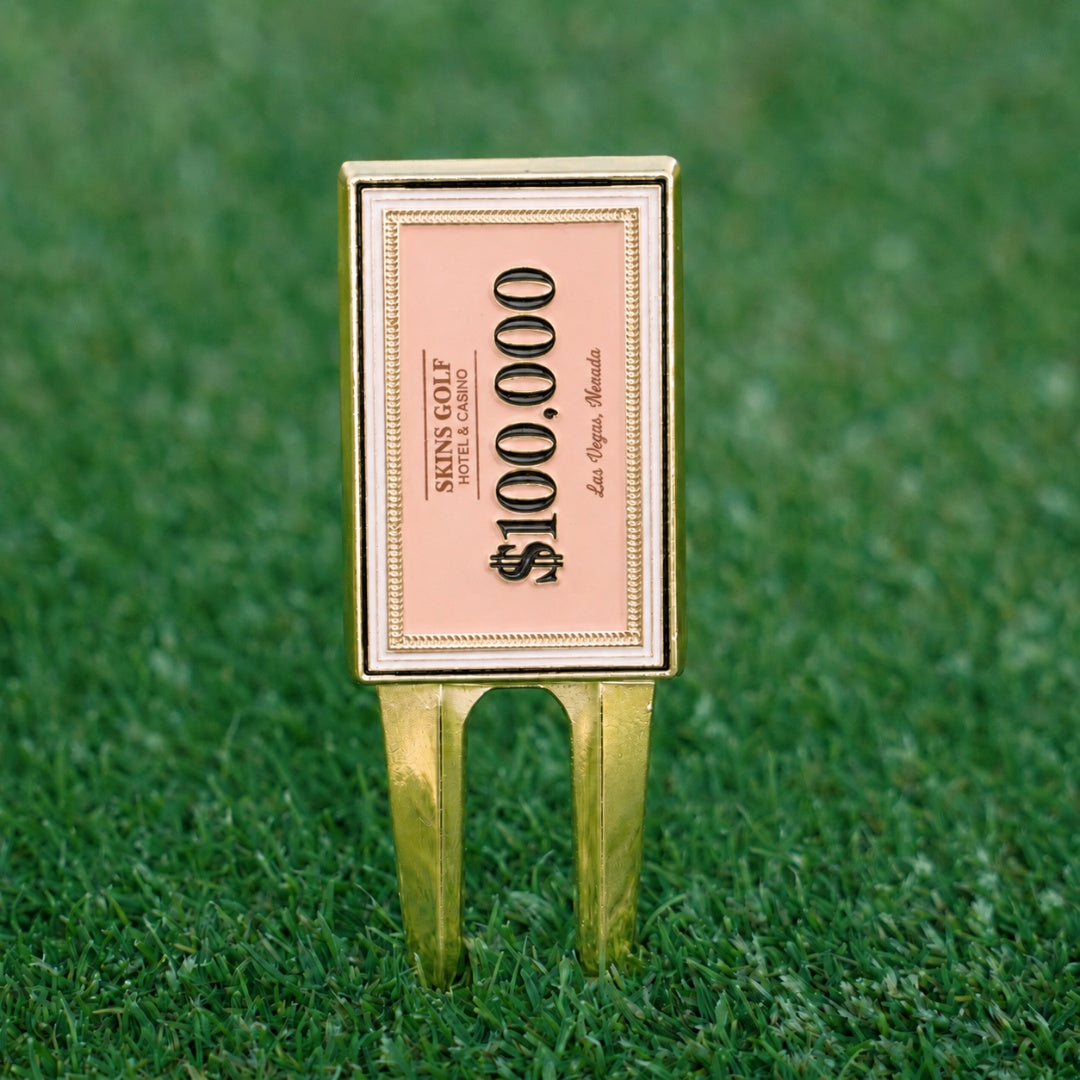 Golf divot tool with $100,000 bill design on a green grass background