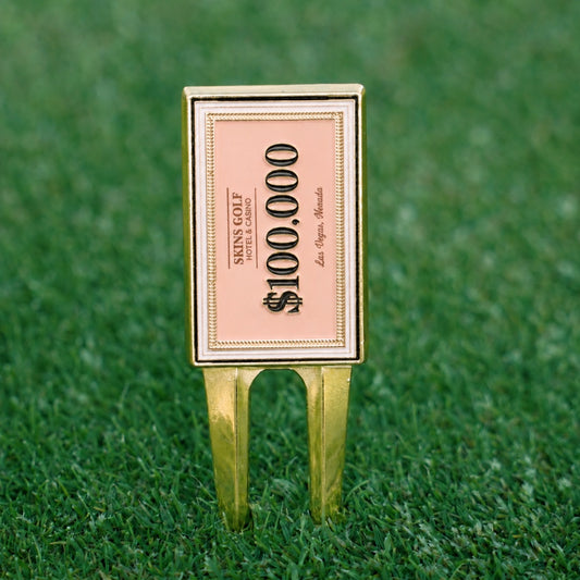 Golf divot tool with $100,000 bill design on a green grass background