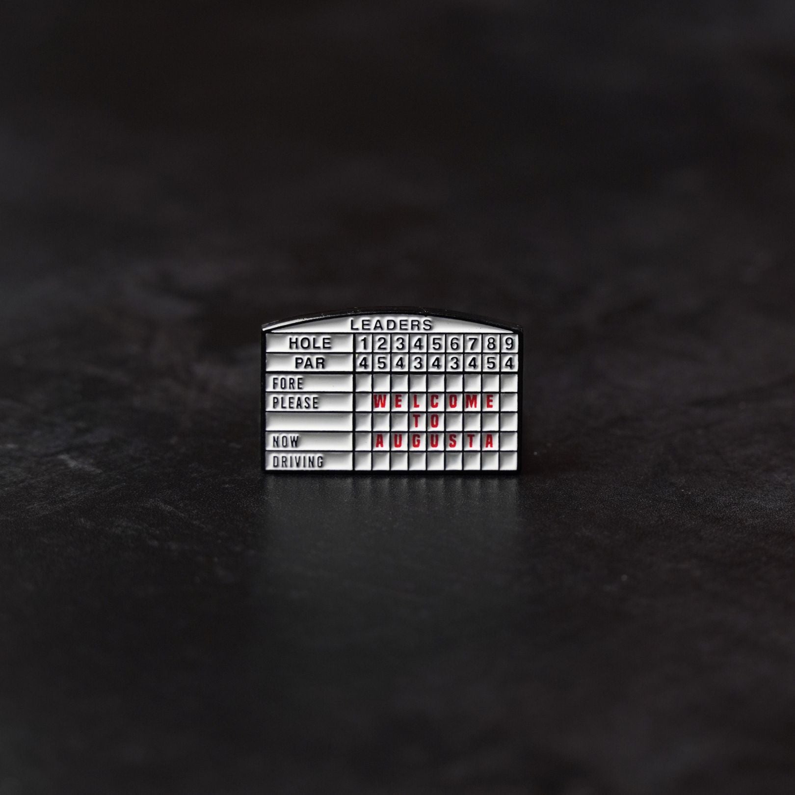 Metal scoreboard golf ball marker on a dark textured background