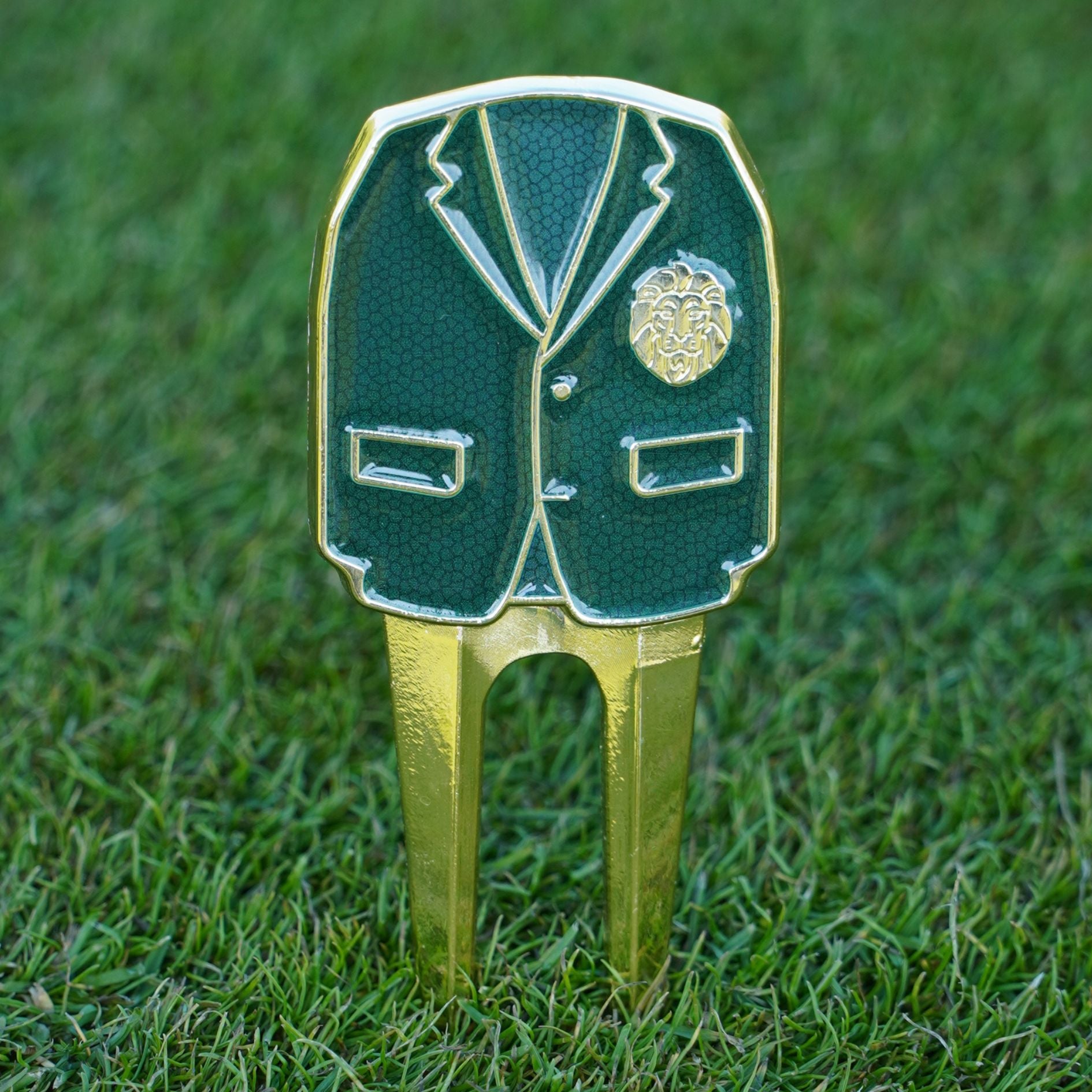 Golf divot tool with green jacket and gold accents on grass