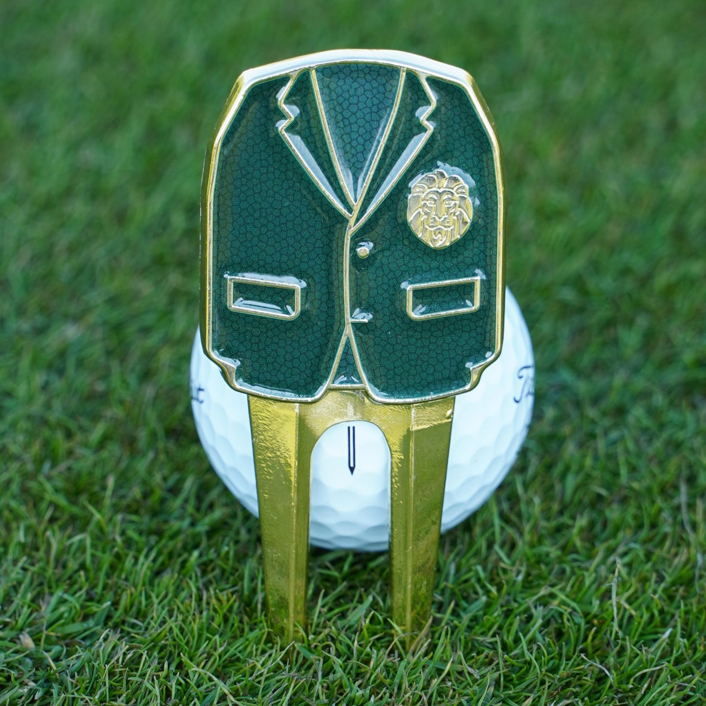 Golf ball with a green blazer and gold divot tool on grass