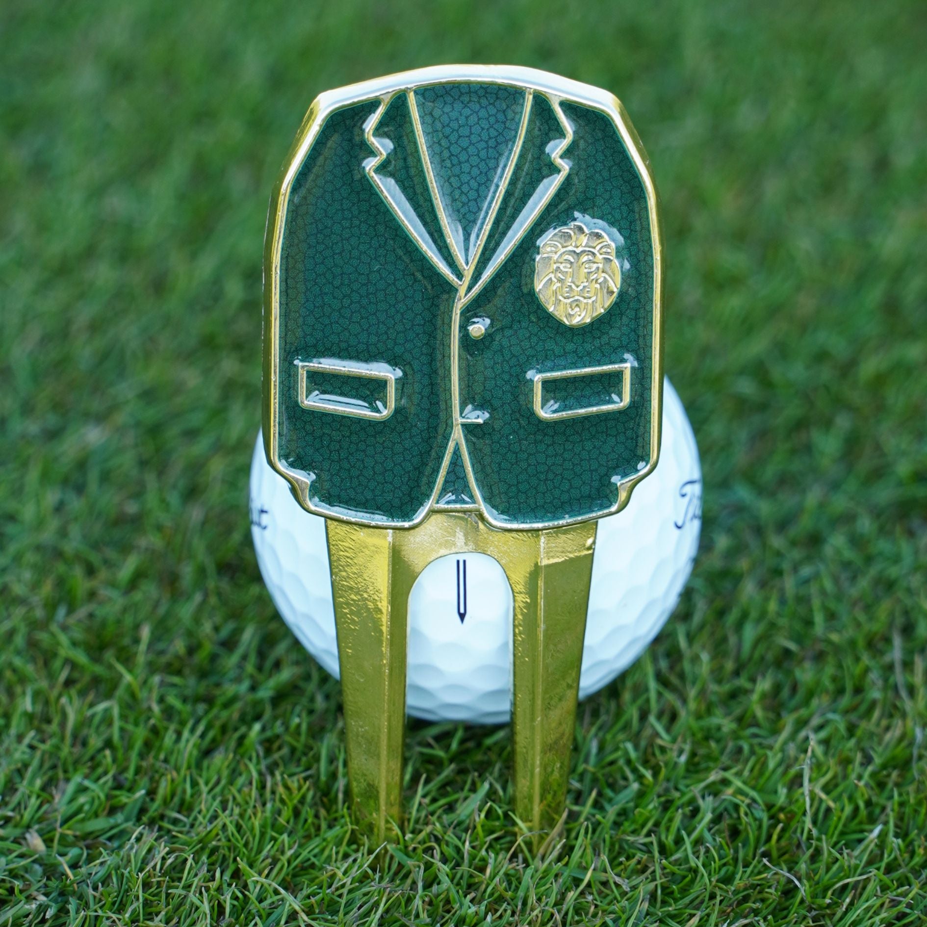 Golf ball with a green blazer and gold divot tool on grass