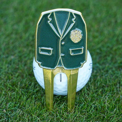 Golf ball with a green blazer and gold divot tool on grass