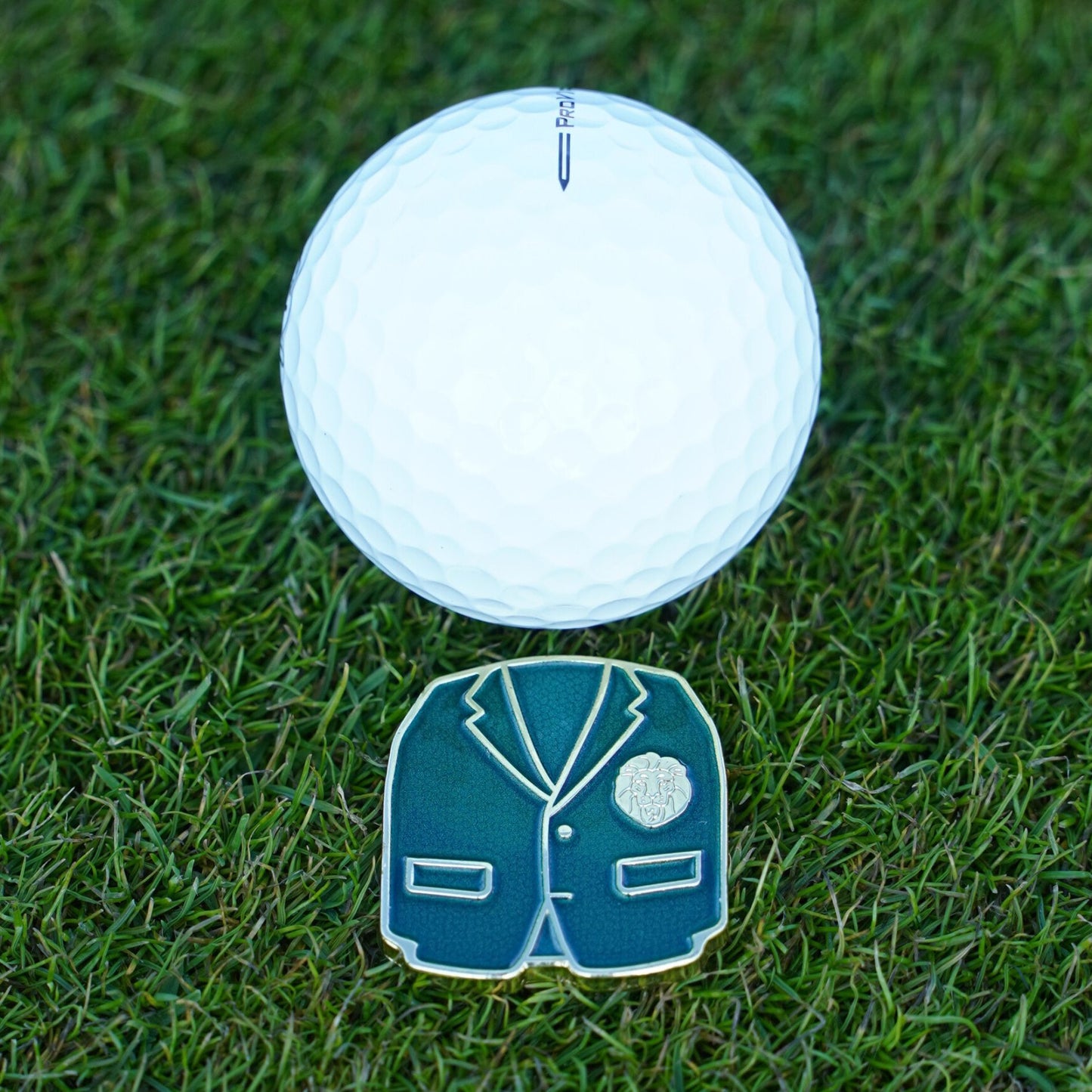 White golf ball on grass with a green jacket ball marker 