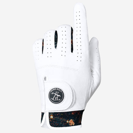 A white golf glove with a black and orange patterned cuff, featuring a circular black and white logo patch on the wrist strap. The glove is shown against a solid light gray background.