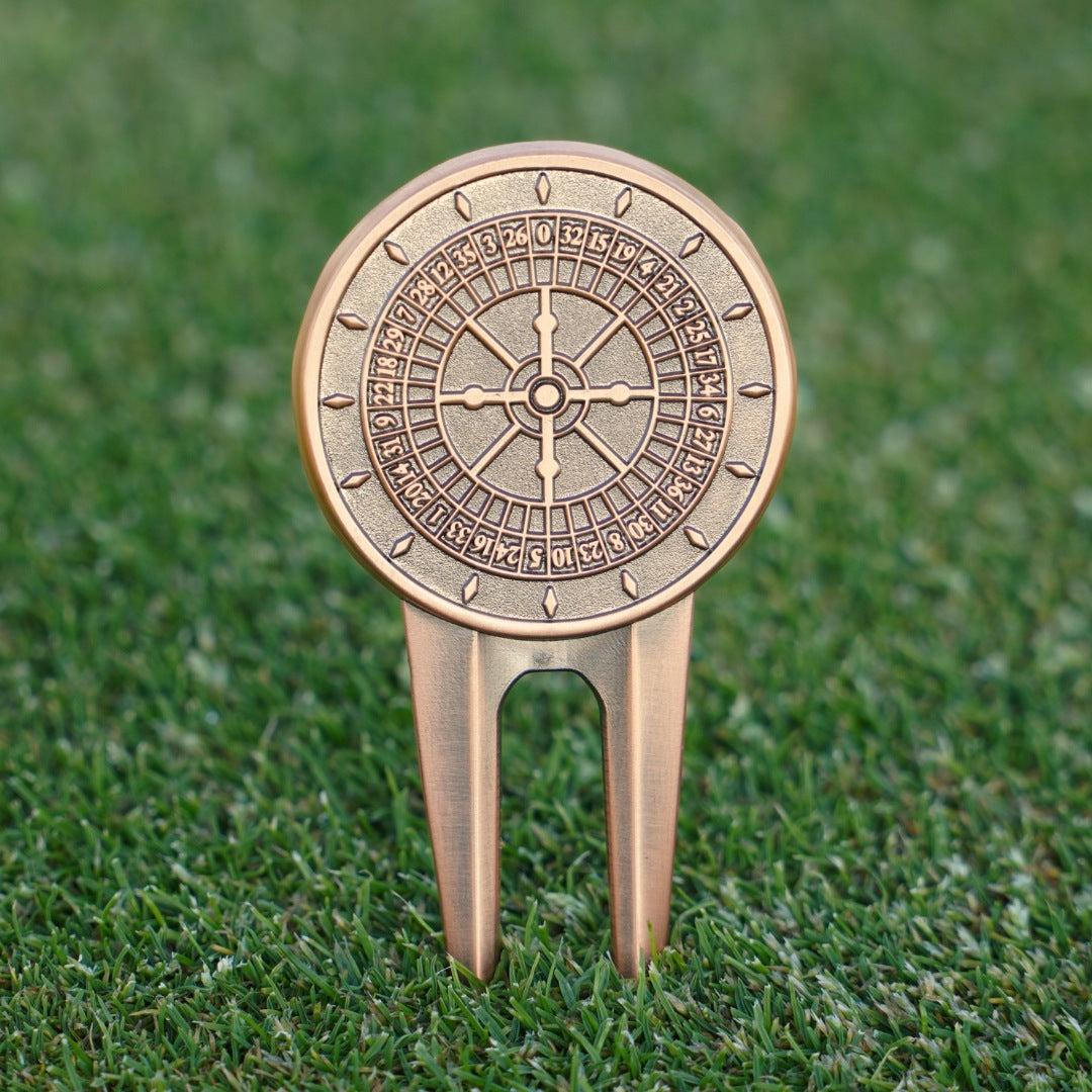 Decorative golf divot tool with roulette design on a grass background