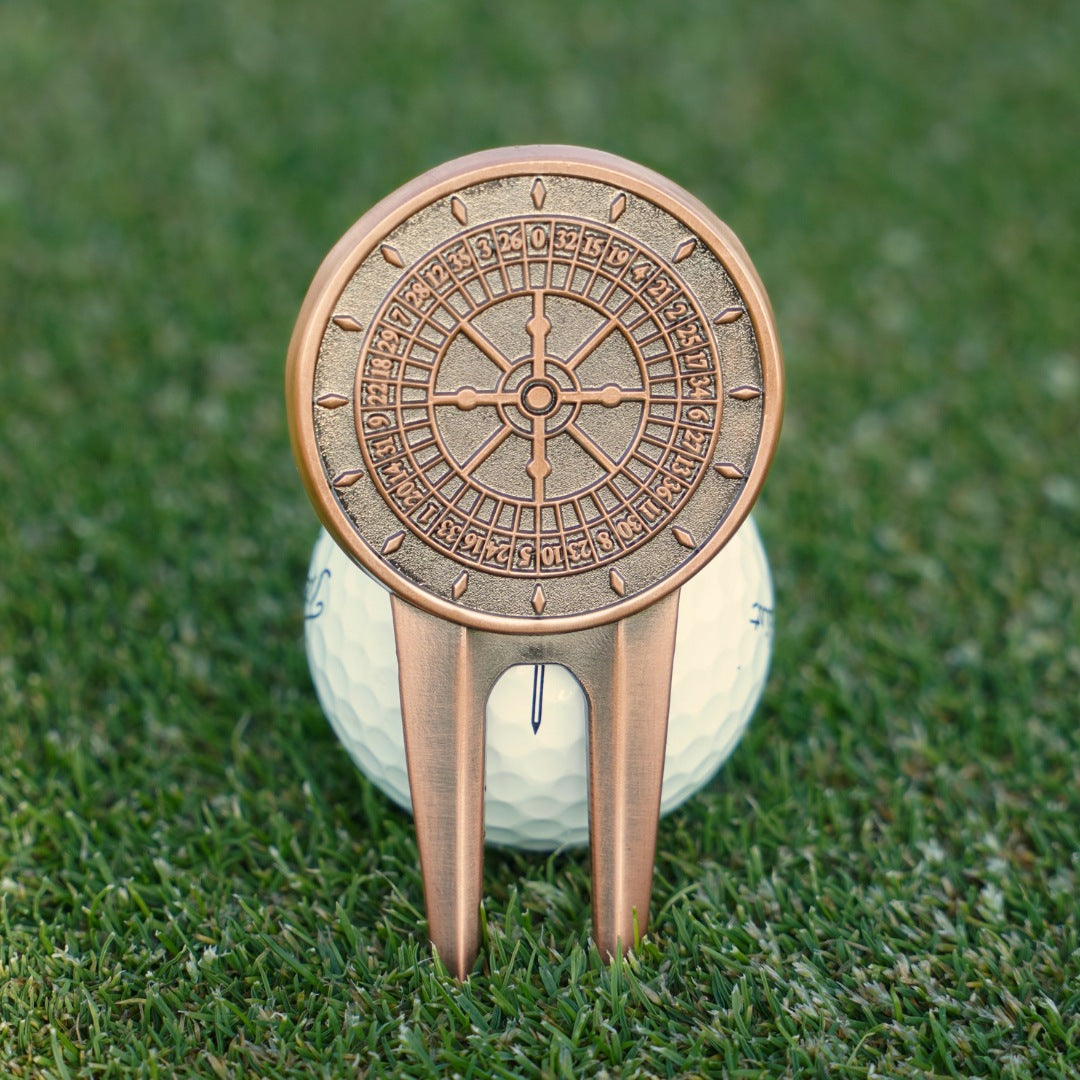 Decorative bronze golf divot tool on a golf ball with a grass background
