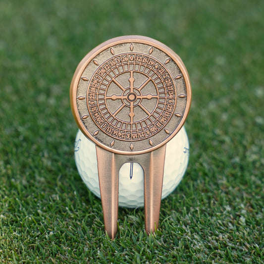 Decorative bronze golf divot tool on a golf ball with a grass background