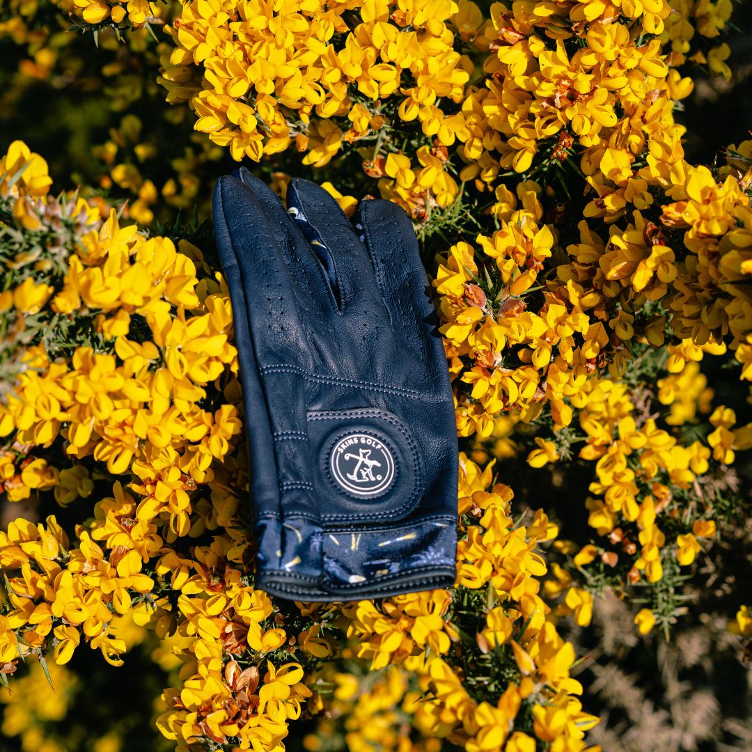 Navy blue leather golf glove with a logo on yellow flowers