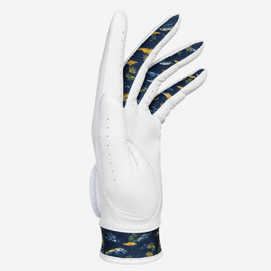 A white golf glove with a navy blue and yellow tropical print on the back of the hand and wrist strap, shown against a light gray background.